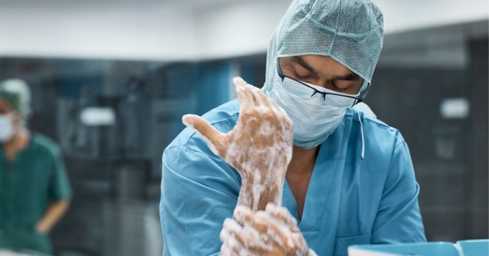 Male doctor wearing scrubs and washing hands thoroughly