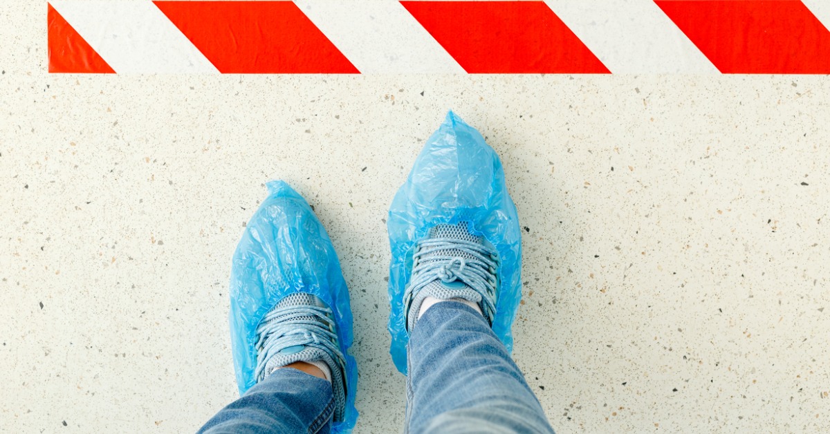 Person standing in line keeping social distance wearing overshoes, medical shoe covers in hospital.