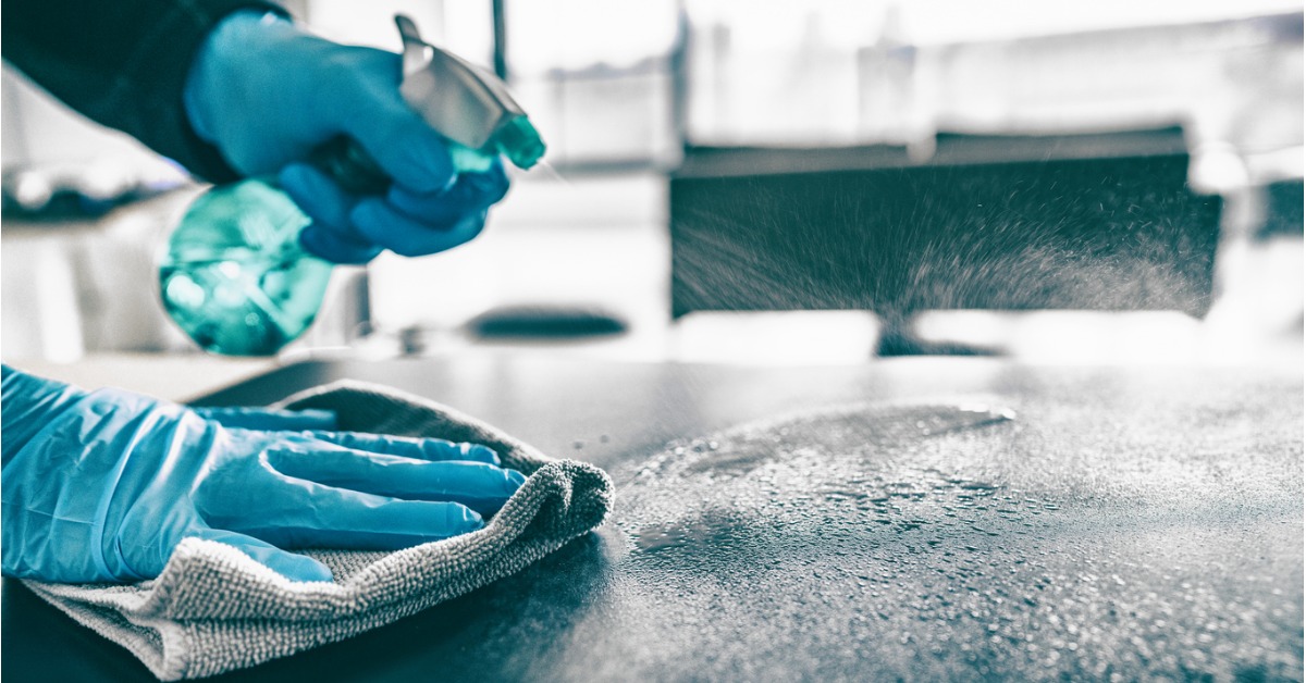 A person with gloves using spray disinfectant to disinfect a hard surface.