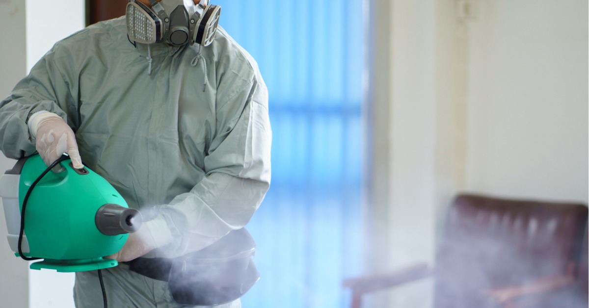 Cleaner in an office environment using a fogging machine for COVID disinfection while wearing the appropriate PPE.