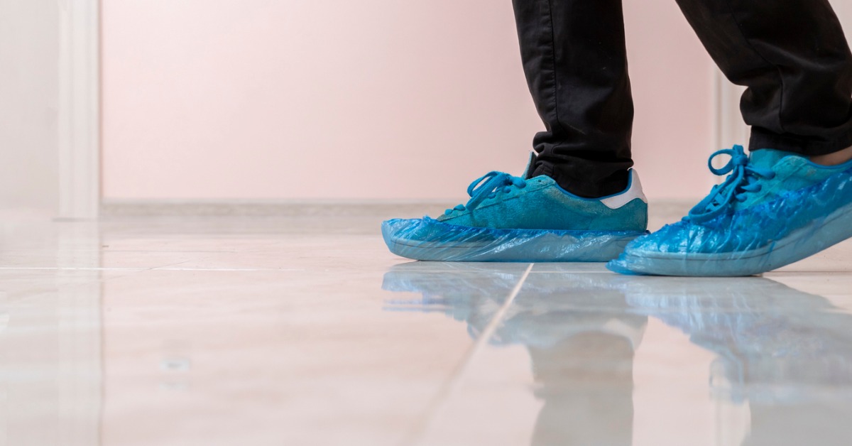 Man walking through an open home after putting shoe covers on using a shoe cover dispenser.