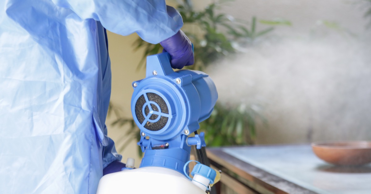 A cleaner in PPE using a fogging machine to disinfect a living room.